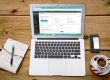 Portátil com o painel do WordPress aberto, junto a um caderno, um telemóvel e uma chávena de café.