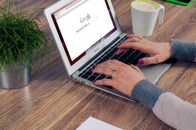 Mãos de uma mulher a pesquisar no Google num computador portátil.
