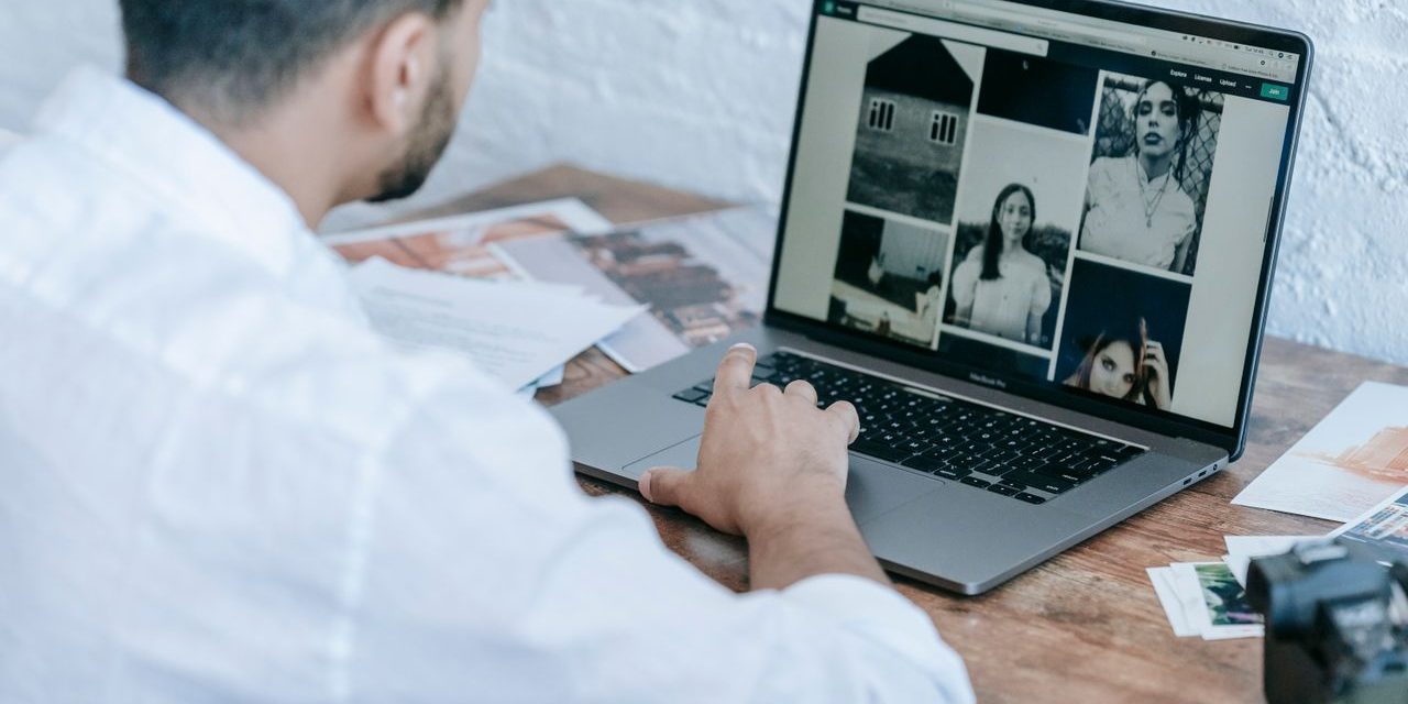 Homem a consultar uma galeria de fotografias num portátil, numa mesa com fotografias impressas e uma câmara.